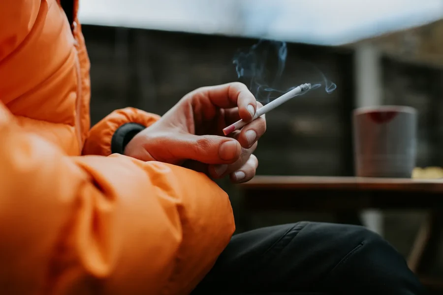 Close-up of a person in an orange jacket holding a cigarette, symbolizing the struggles linked to Adderall addiction and stimulant misuse.