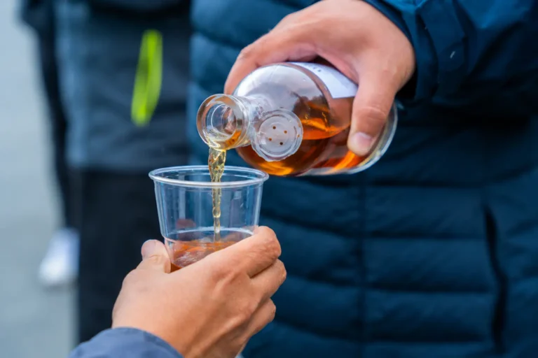 Person heller alkohol fra lommelerke i plastkopp utendørs