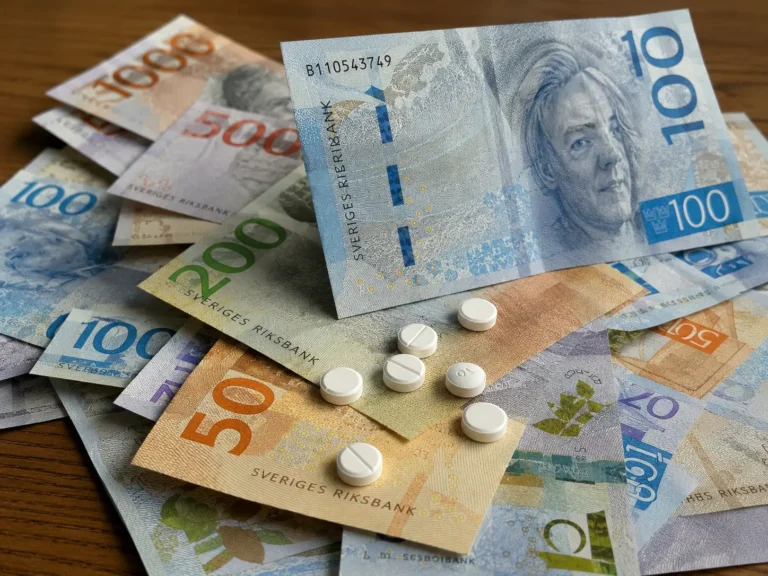 Hvide runde tabletter spredt ud over svenske sedler på et bord, der illustrerer amfetaminmisbrug i en skandinavisk kontekst