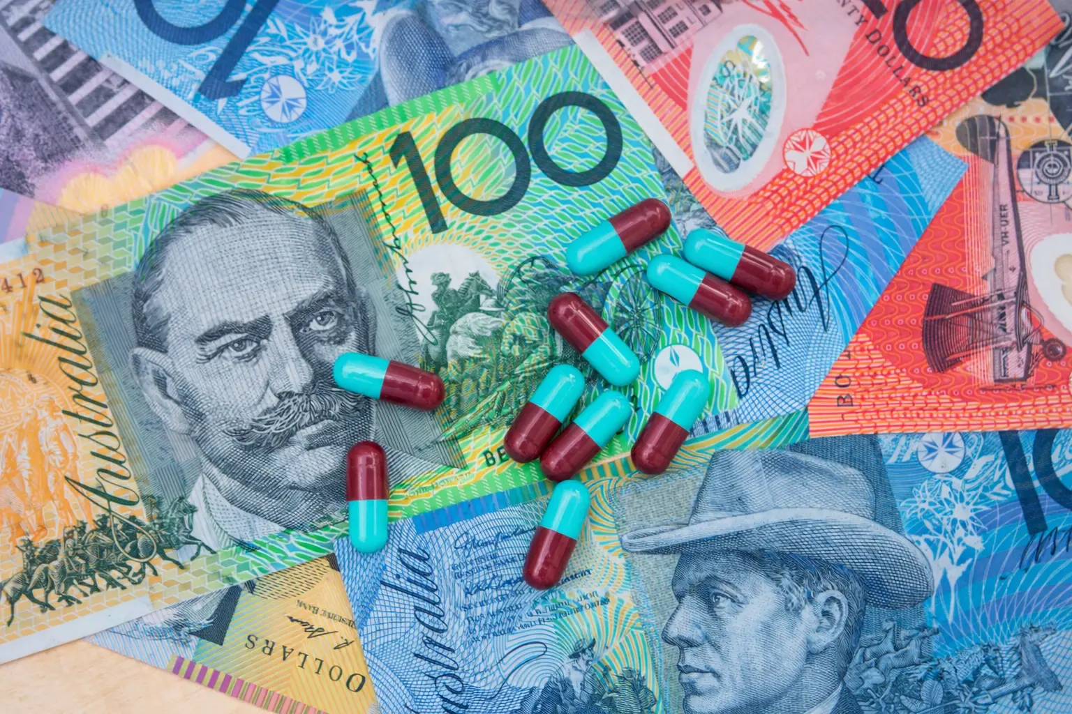 Red and teal pharmaceutical capsules placed on Australian dollar banknotes, representing the financial cost of addiction treatment and medication.