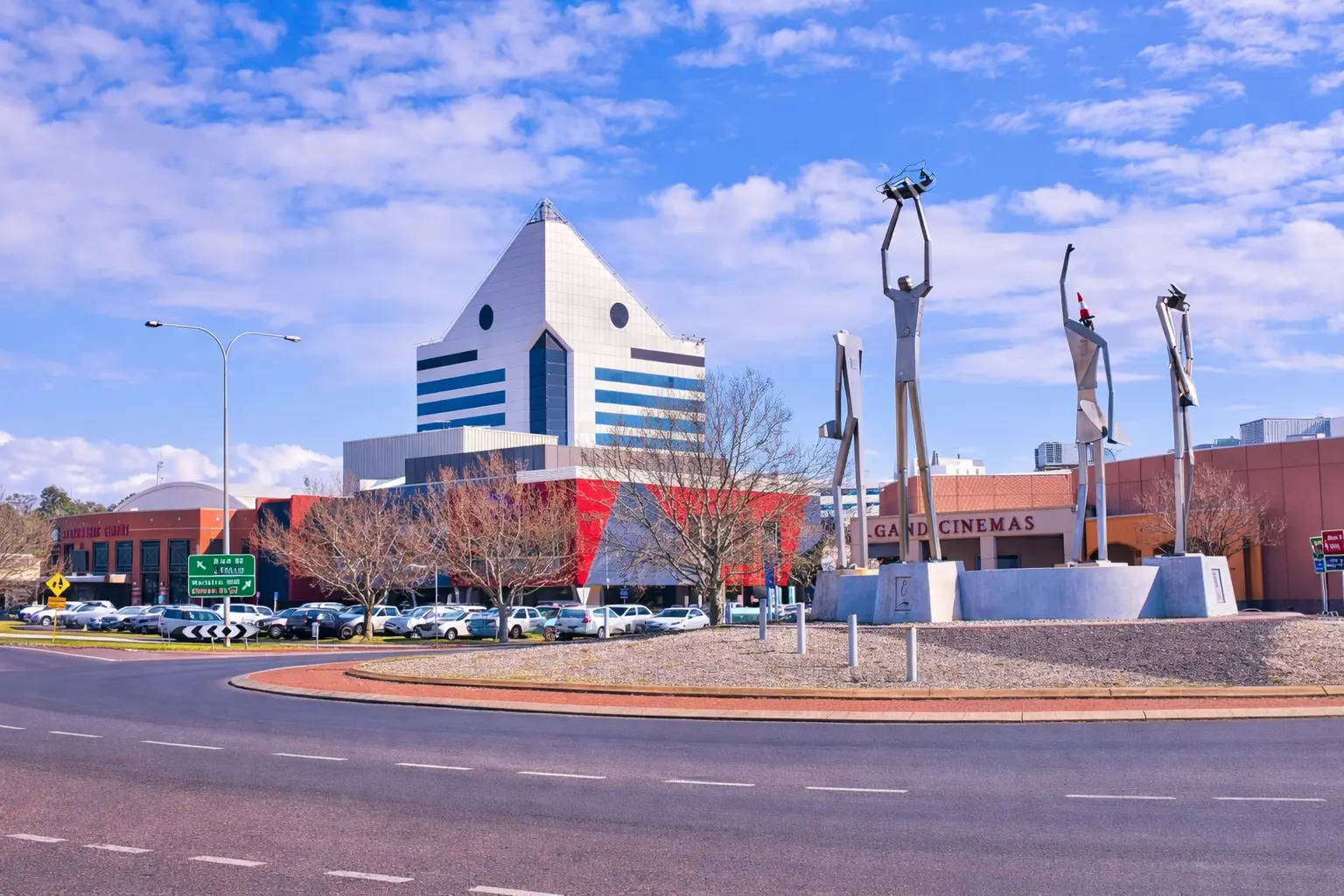 Urban center in Australia with a modern pyramid-shaped building and public sculptures near a roundabout, representing a domestic city setting where local health and community services are accessed.