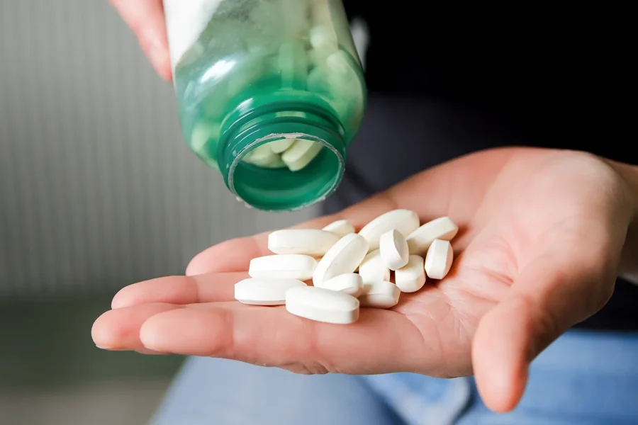 Close-up of a hand holding several white pills poured from a bottle, symbolizing benzodiazepine addiction and dependence.