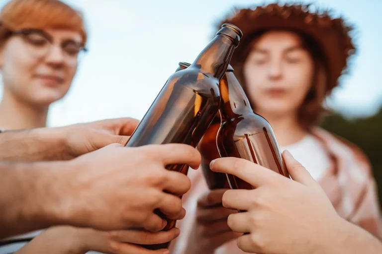 Group of friends clinking beer bottles — symbol of binge drinking, treatment at Siam Rehab