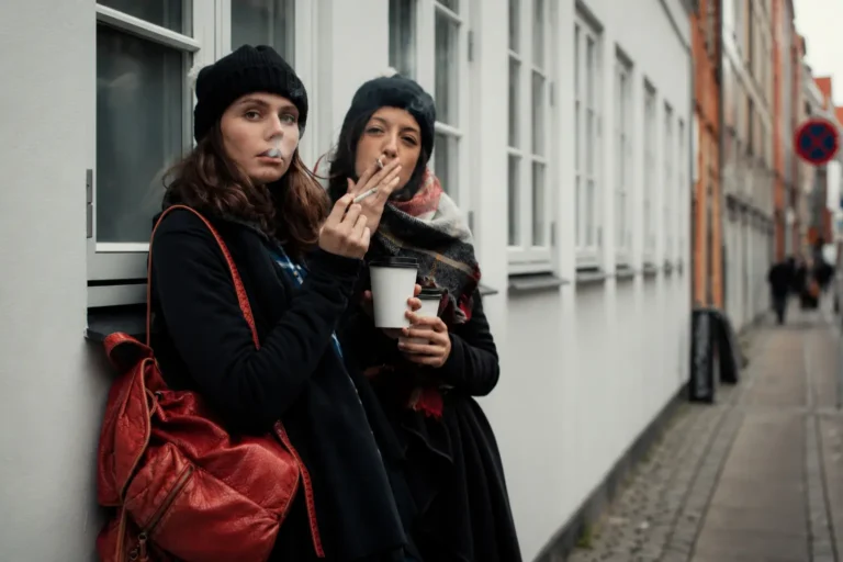 To unge kvinder ryger på en gade i København, der illustrerer det sociale cannabisbrug integreret i dansk hverdagsliv