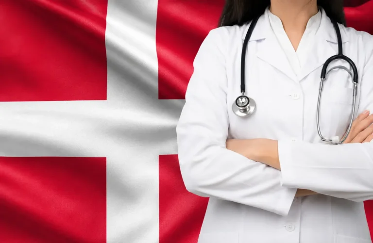 Læge med stetoskop og foldede arme foran det danske flag, der illustrerer dansk sundhedsforsikring og misbrugsbehandling