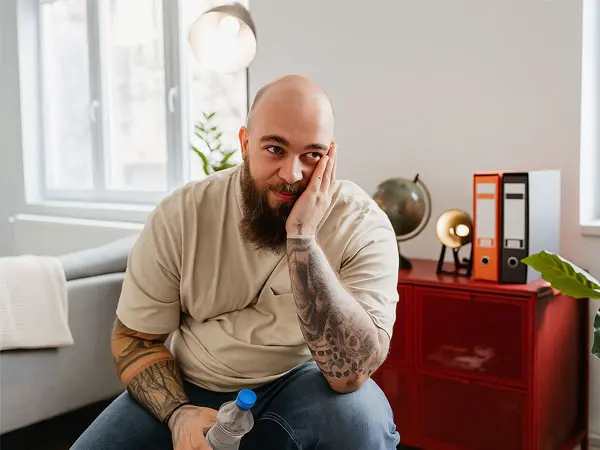 Man with tattoos sitting in a room, looking distressed, symbolizing the struggles of drug abuse.