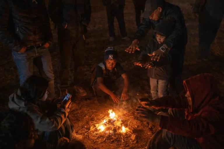 A group of individuals huddling around a campfire at night to warm their hands, symbolizing the communal stabilization and transition from crisis to a structured environment during the first week of rehab.