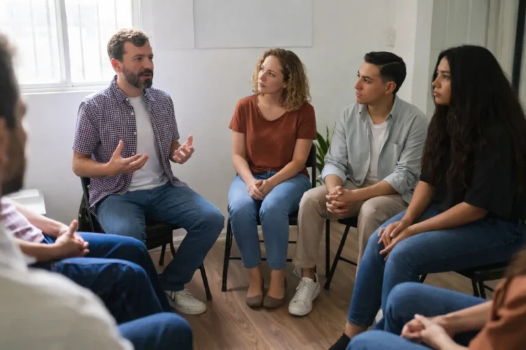 Small group therapy session with a facilitator speaking to seated participants in a clinical discussion setting.
