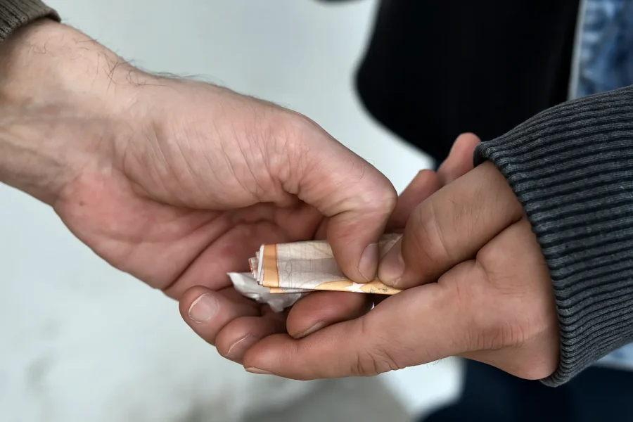 Close-up of hands exchanging money in a street deal, symbolizing the hidden dangers of heroin addiction.
