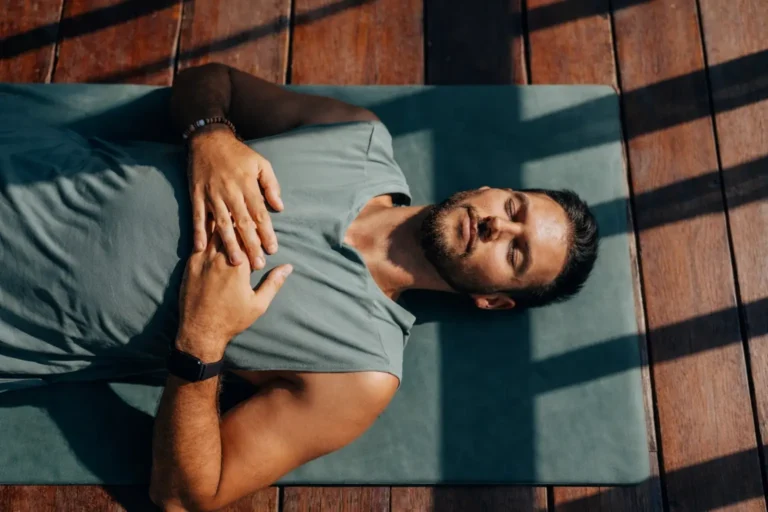 A man lying on a yoga mat with his hands on his chest at a residential recovery facility, demonstrating psychological stability.