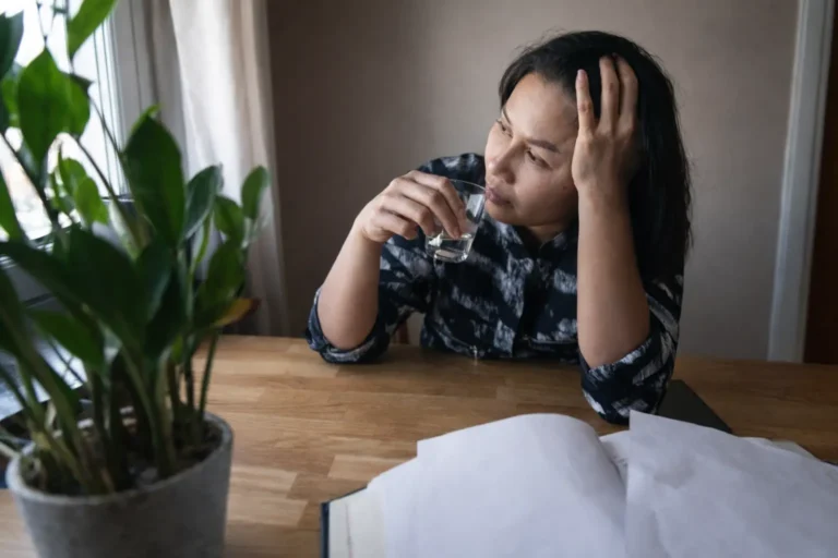 Person sitting at a table holding a glass and looking fatigued, representing early risk escalation, loss of control patterns, and the decision threshold for family intervention timing.