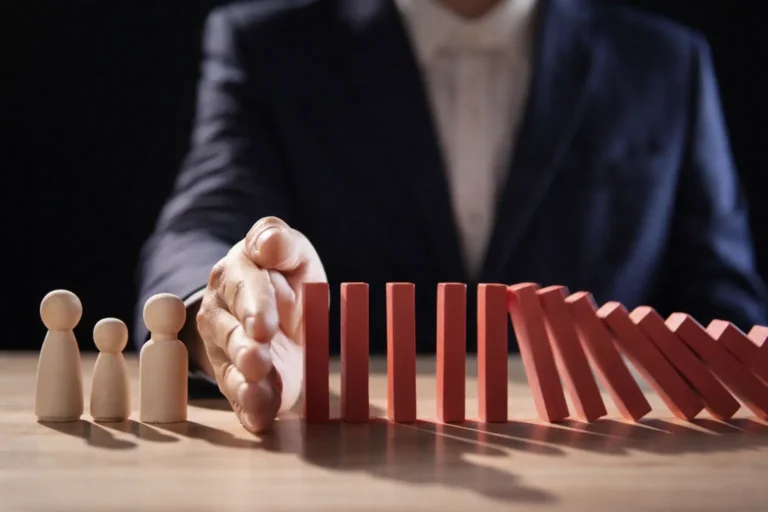 Hand stopping falling dominoes to protect wooden family figures, symbolizing legal intervention or forced rehab to halt addiction escalation.
