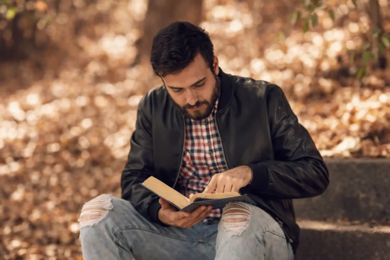 A man sits on outdoor steps in a quiet wooded area reading a book, representing a calm recovery setting.