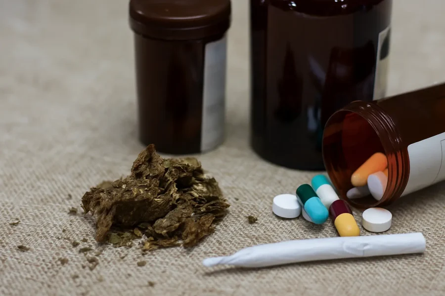 Close-up of marijuana, rolled joint, and scattered pills on a table, symbolizing marijuana addiction and drug dependence.