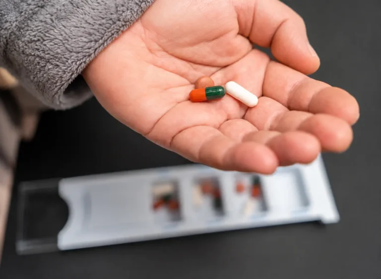Hand holding medication capsules from a weekly pill organizer illustrating medication management challenges in outpatient addiction treatment