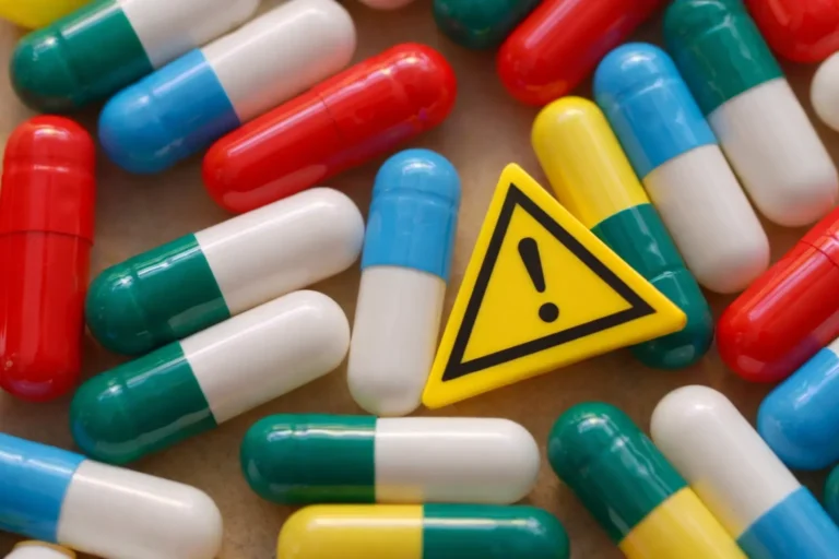 Assorted pharmaceutical capsules with a warning symbol indicating medication risk and clinical supervision requirements.