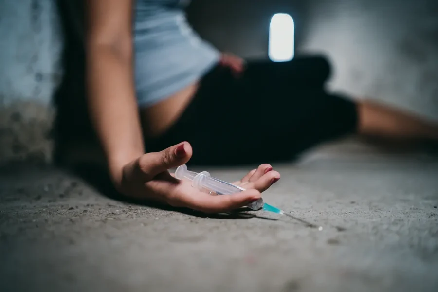 Person lying on the ground with a syringe in hand, symbolizing the devastating effects of meth addiction.
