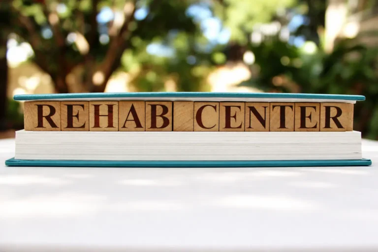 Wooden blocks spelling "REHAB CENTER" inside a book, representing the practical and administrative preparation needed for residential recovery.