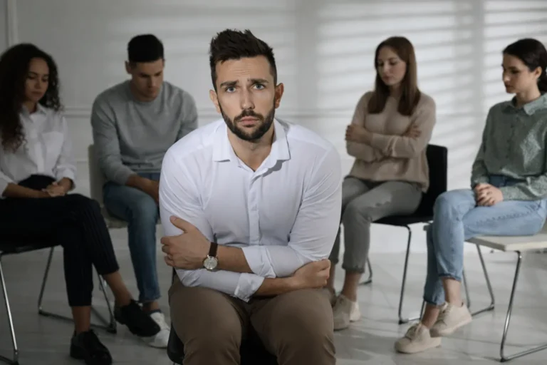 Man seated at the front of a group therapy session with other participants behind him, illustrating evaluation of outpatient rehabilitation limits and need for higher-intensity care in Australia.