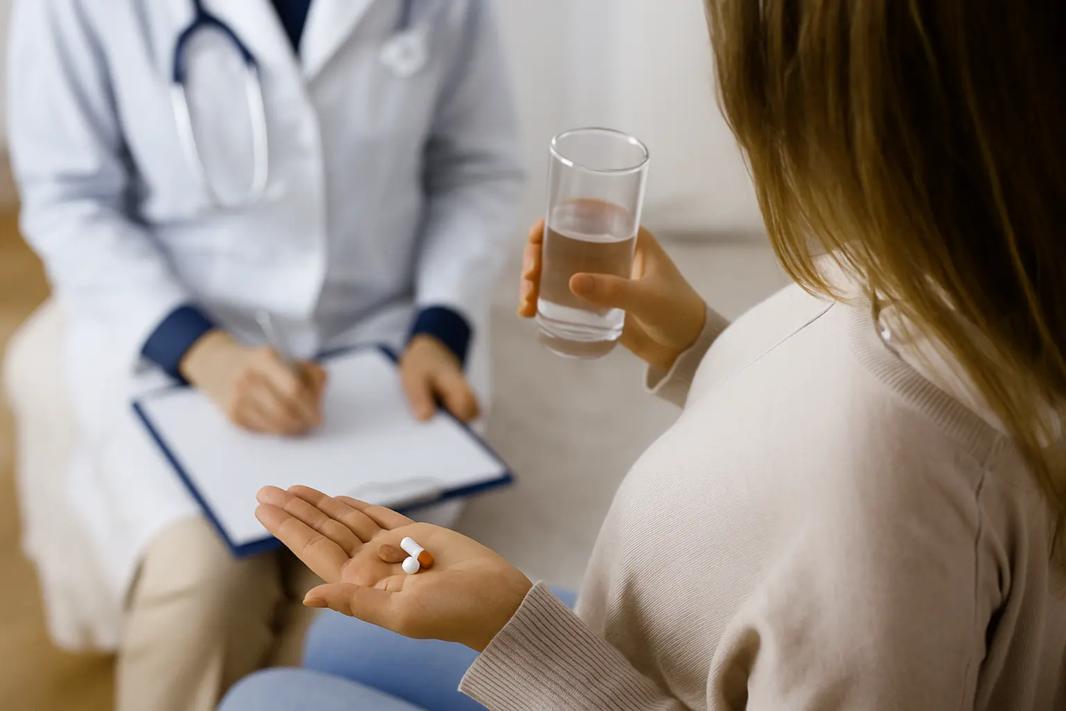 A patient gestures with open hands while speaking to a clinician who holds a clipboard during a behavioral health assessment.