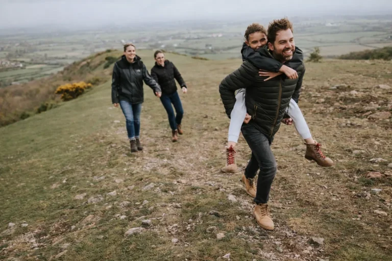 A family enjoying a hike on a grassy hill, representing the restoration of relationships and healthy shared activities during recovery stabilization.