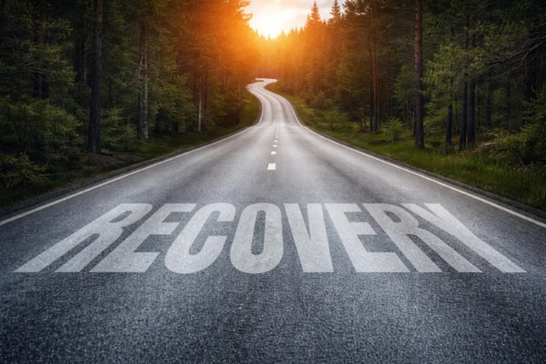 Forest road stretching toward a sunrise with the word Recovery painted on the pavement, symbolising structured rehabilitation and long term recovery.