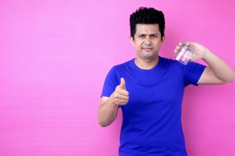Man holding a glass of alcohol while giving a conflicted thumbs-up gesture, symbolizing denial, ambivalence, and resistance to acknowledging substance-related harm.