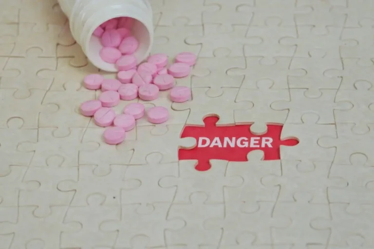 Pink pills spilling from a bottle onto a white jigsaw puzzle with a missing piece revealing the word Danger in red, symbolizing the immediate risks of addiction relapse.