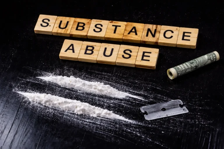 Wooden letter blocks spelling out substance abuse alongside white powder lines, a razor blade, and rolled currency on a dark background.