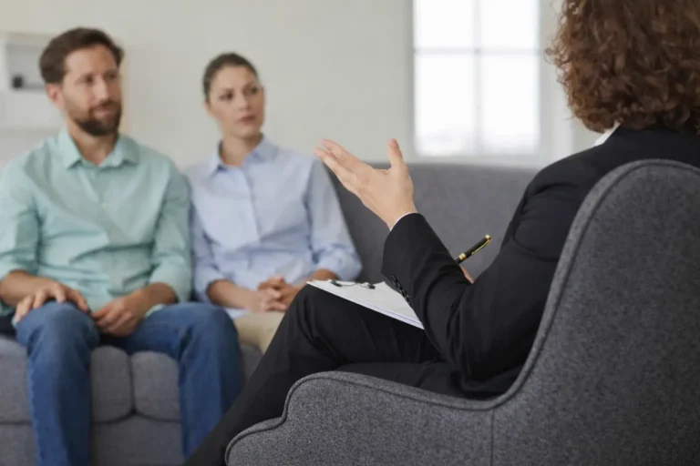 Therapist conducting a consultation session with a couple seated on a sofa in a clinical setting.