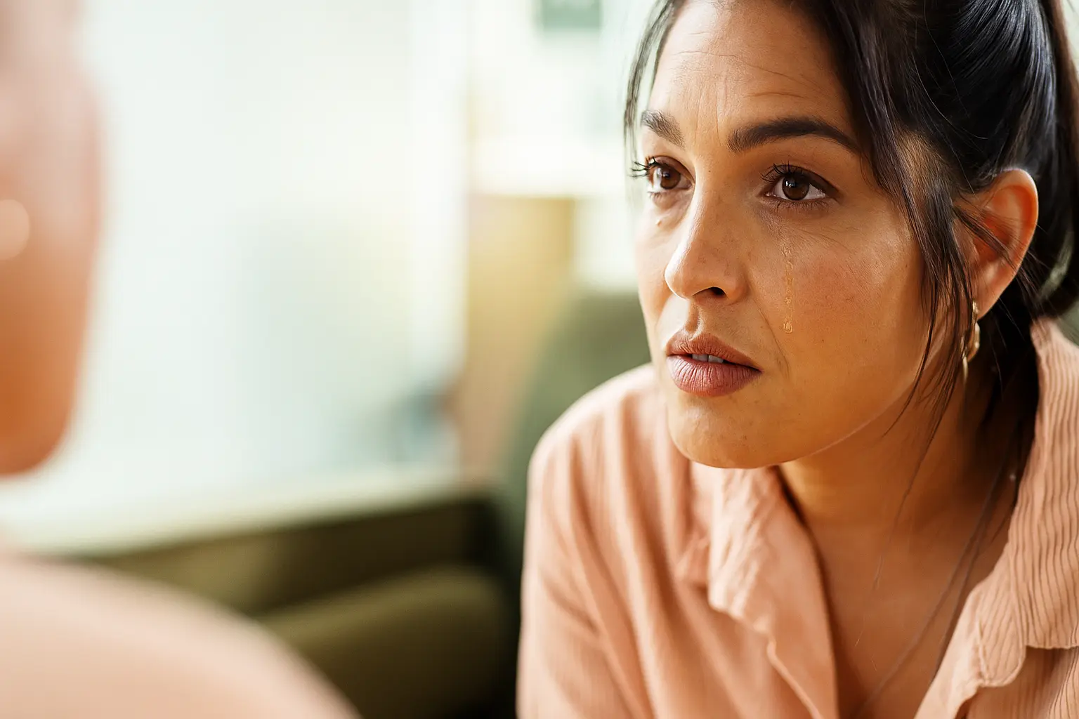 A woman with tears on her cheek listens intently during an emotional conversation, representing the pain of addiction, family struggles, and the importance of compassionate support at Siam Rehab.