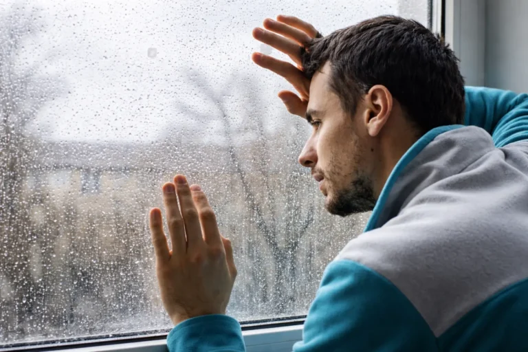 Applicant leaning against a rain-covered window, appearing worried and reflective, representing uncertainty and emotional stress during treatment screening decisions