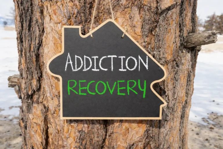 Chalkboard sign reading addiction recovery attached to a tree, symbolizing a transition toward structured recovery, environmental change, and a defined treatment window away from triggering environments.